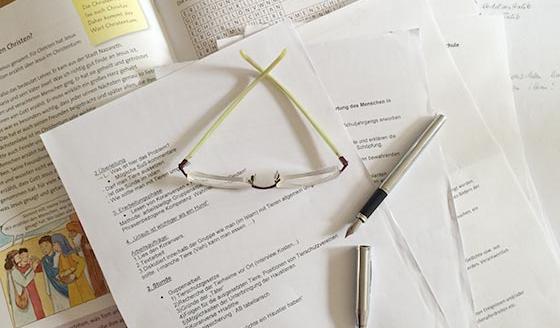 Gutachterische Tätigkeiten Füllhalter und Brille auf Papieren zum Thema Religionsunterricht
